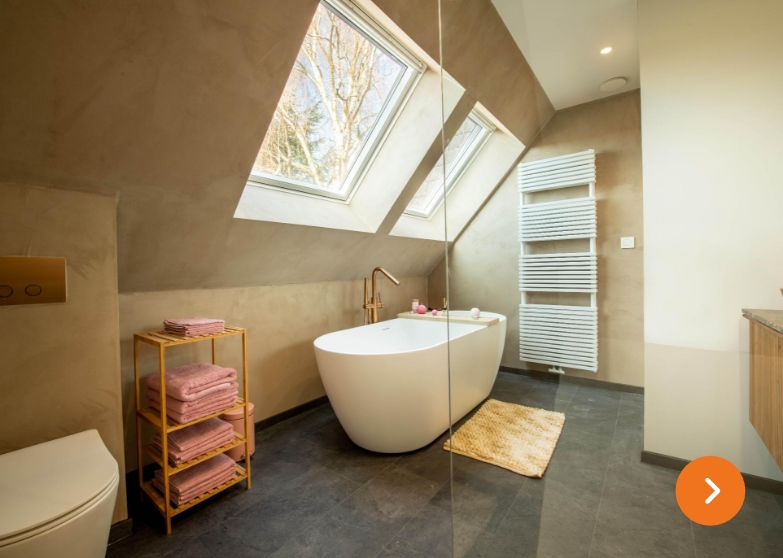 Gezellige badkamer onder een schuin dak, met vrijstaand bad en roze handdoekenrekje